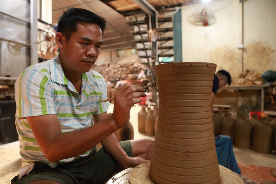 Nghệ nhân chạm khắc những đường nét lên thân gốm. (Ảnh: PV/Vietnam+)
