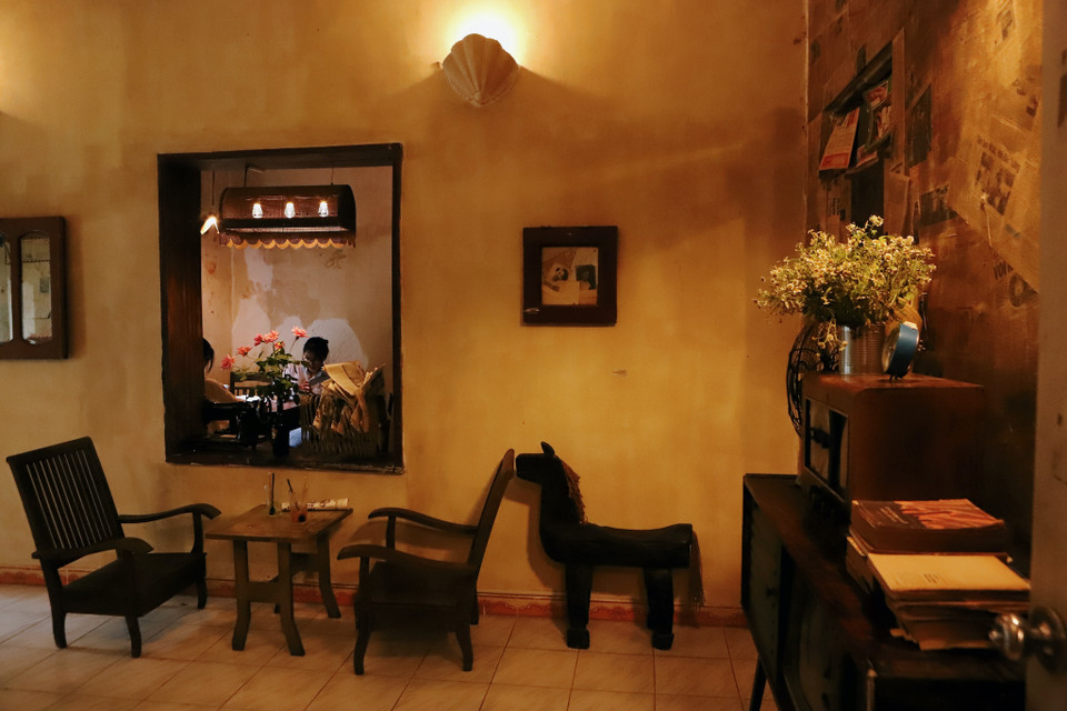 Nơi đây có không gian rất thiên nhiên cùng những bộ bàn ghế gỗ mộc mạc và lớp tường tróc sơn tái hiện lại đúng thời bao cấp. Bước chân vào không gian bên trong, bạn sẽ thấy như đang trở về lịch sử, nơi mà tưởng như ta chỉ được hình dung qua sách vở. (Ảnh: Quỳnh Anh/Vietnam+)