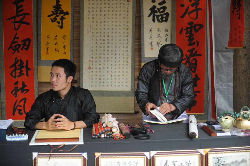 Vắng khách, một ông đồ tranh thủ mở từ điển ra đọc lại chữ. (Ảnh: Minh Sơn/Vietnam+)