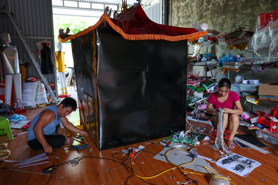 Gia đình anh Bùi Trọng Công có kinh nghiệm hơn 10 năm làm nghề đang ngồi cắt dán, đính từng chi tiết căn nhà âm phủ. Anh Công cho biết để hoàn thiện một công trình lớn anh và vợ mất nguyên một ngày nhưng giá bán buôn chỉ từ 2-300 nghìn đồng/sản phẩm. (Ảnh: Minh Sơn/Vietnam+)