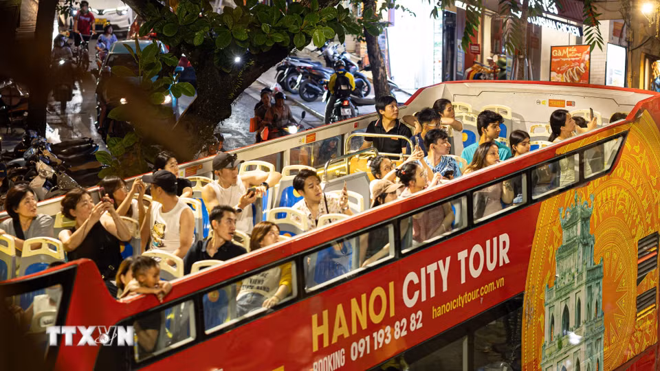 Đông đảo du khách trong và ngoài nước thích thú ngắm nhìn toàn cảnh không gian Hà Nội về đêm từ không gian mở trên tầng 2 của xe bus du lịch (Hanoi City Tour). Việc đưa vào vận hành và đẩy mạnh các tour ngắm cảnh đêm (Night Tour) bằng phương tiện hiện đại không chỉ làm đa dạng hóa các lựa chọn trải nghiệm cho du khách khi thành phố lên đèn, mà còn đóng vai trò như một "mạch máu" giao thông kết nối hiệu quả các điểm đến di sản văn hóa, ẩm thực và thương mại sầm uất trong chuỗi hệ sinh thái kinh tế đêm của Thủ đô. (Ảnh: Tiến Long/TTXVN phát)