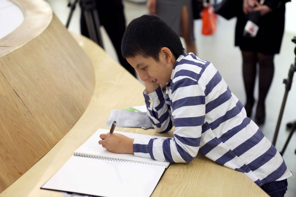 Cậu bé này có biệt danh là Nem (một trong số các bé bị tự kỷ có bộ ảnh trong triển lãm) hồn nhiên thể hiện tài năng hội họa của mình ngay trong triển lãm. (Ảnh: Doãn Đức/Vietnam+)