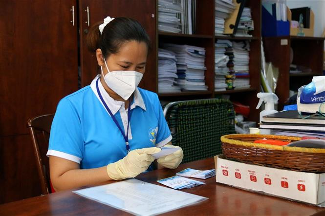 Chủ tịch Hội Liên hiệp phụ nữ Quận 3 Đoàn Thị Cẩm Tú làm thêm thẻ tình nguyện viên cho hội viên phụ nữ phường đi chợ giúp dân mua hàng hóa, lương thực trong những ngày thực hiện giãn cách xã hội. (Ảnh: Thanh Vũ/TTXVN)