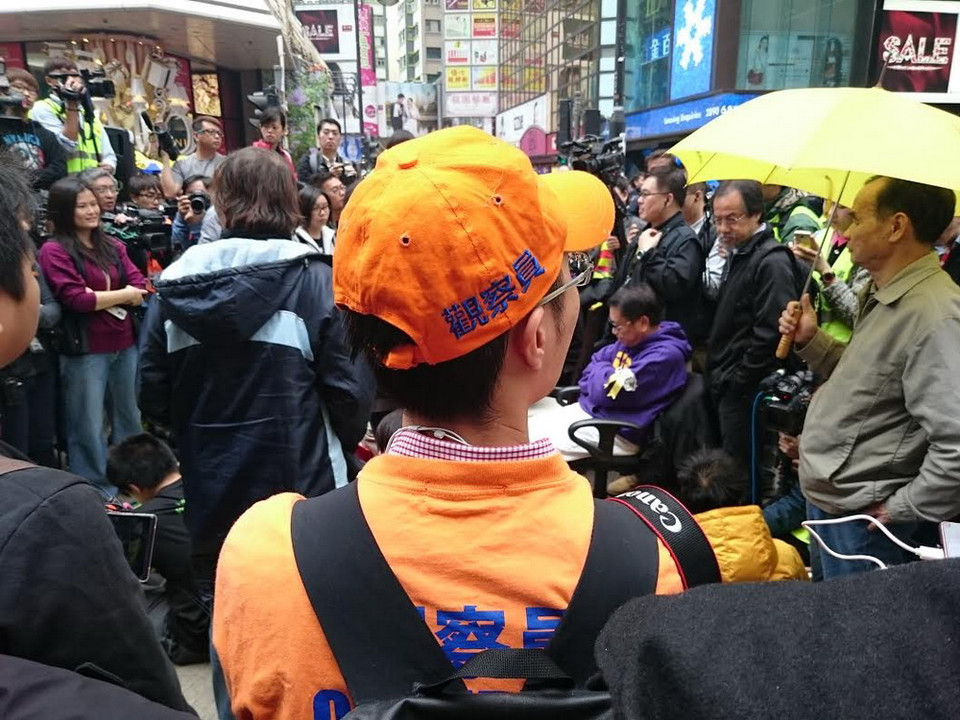 Các nhân viên quan sát (áo màu cam) có mặt tại Causeway Bay để giám sát quá trình thực thi nhiệm vụ của các lực lượng chức năng. (Ảnh: Hà Ngọc/TTXVN)