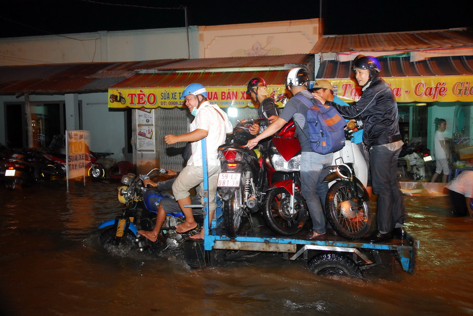 Nhiều xe ba gác máy vận chuyển xe máy của người dân qua điểm ngập sâu. (Ảnh: Mạnh Linh/TTXVN) 