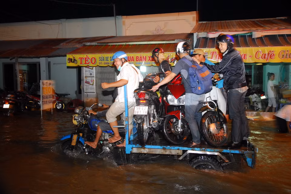 Nhiều xe ba gác máy vận chuyển xe máy của người dân qua điểm ngập sâu. (Ảnh: Mạnh Linh/TTXVN) 