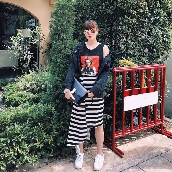 Trưng dụng áo tank in hình và chân váy kẻ ngang bất đối xứng, Yến Nhi biến tấu ngẫu hứng set đồ dạo phố khi thêm denim khoác ngoài, giày thể thao khỏe khoắn và kính mắt tráng gương thời thượng.