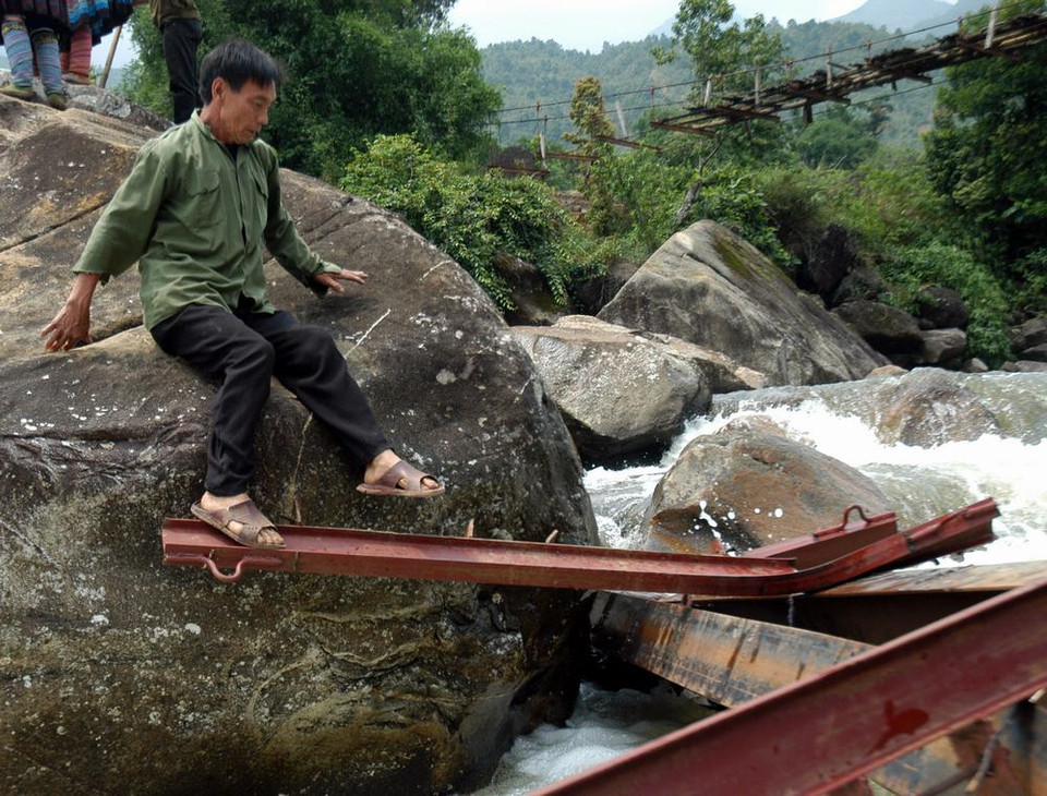  Người dân Chu Va 6 vượt qua suối trên những thanh sắt cầu tạm vừa bị lũ cuốn trôi rất nguy hiểm đến tính mạng. (Ảnh: Nguyễn Công Hải/TTXVN)