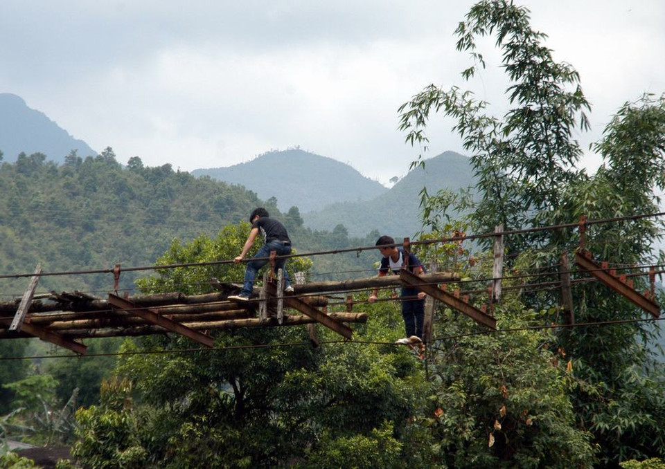 Nhiều người dân vượt qua suối trên chiếc cầu treo cũ nát bỏ hoang rất nguy hiểm. (Ảnh: Nguyễn Công Hải/TTXVN)