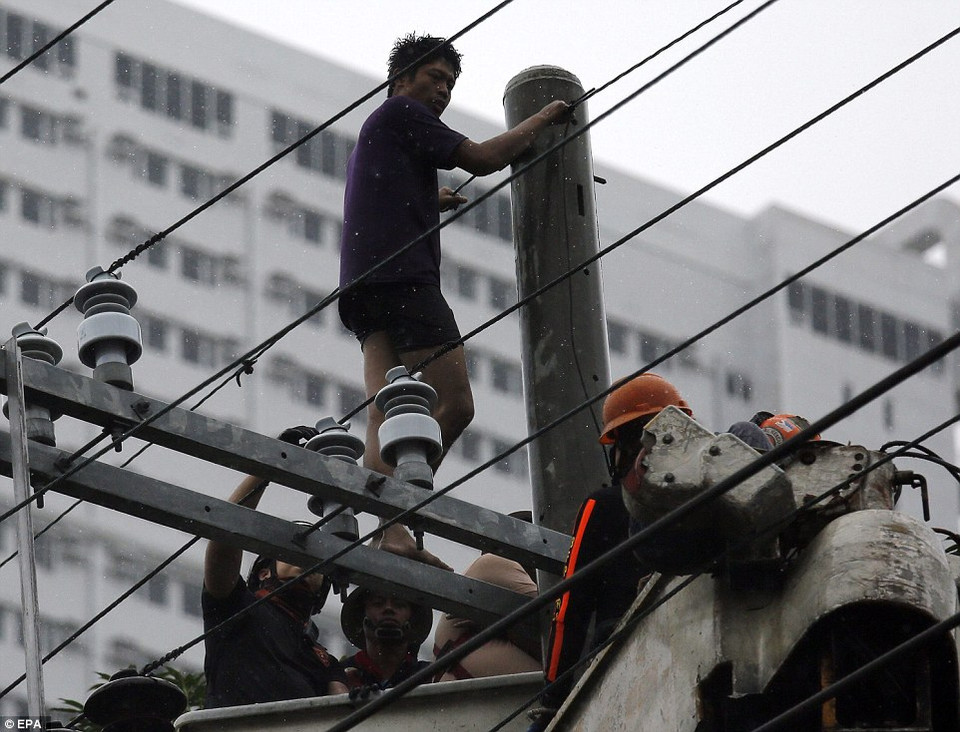 Một nghi phạm do quá sợ hãi mà leo lên cột điện, các nhân viên cứu hộ đang thuyết phục hắn leo xuống. (Nguồn: Dailymail)