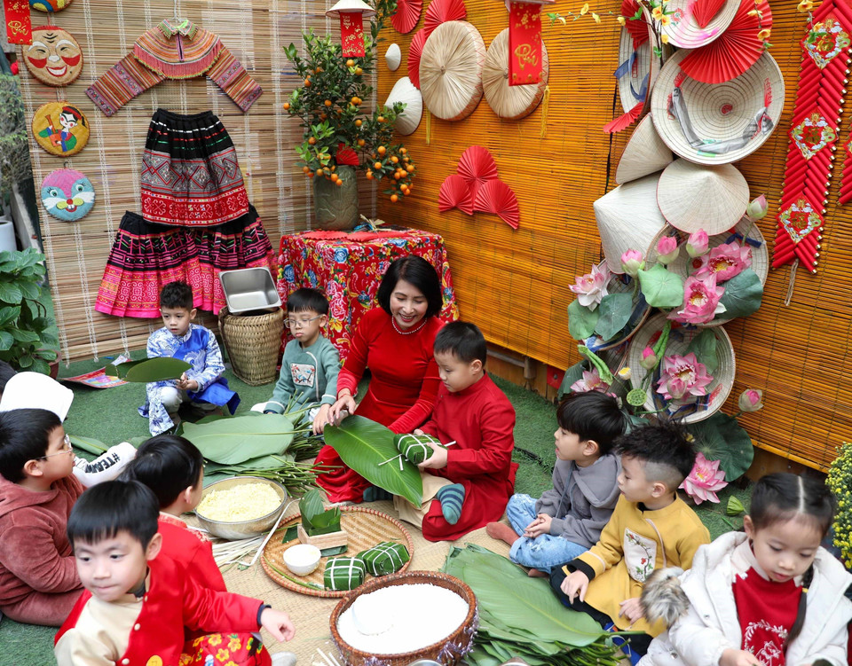 Cô giáo hướng dẫn trẻ cùng gói bánh chưng. (Ảnh: Thanh Tùng/TTXVN)