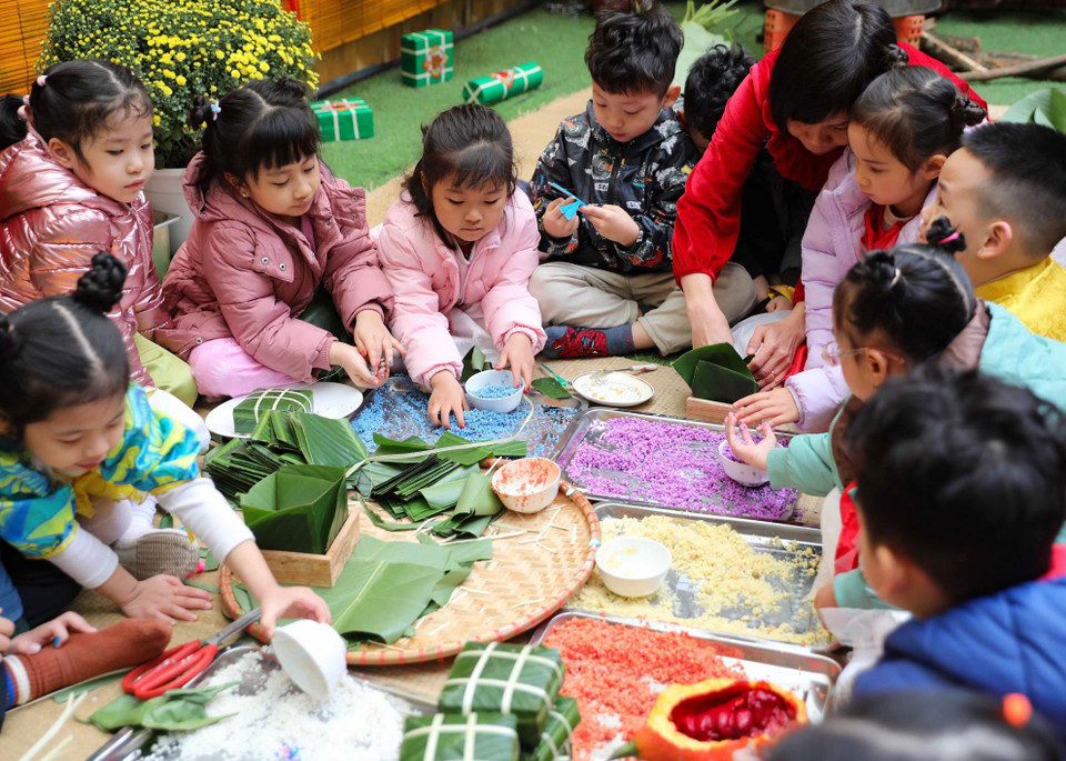 Cô giáo hướng dẫn trẻ cùng gói bánh chưng. (Ảnh: Thanh Tùng/TTXVN)