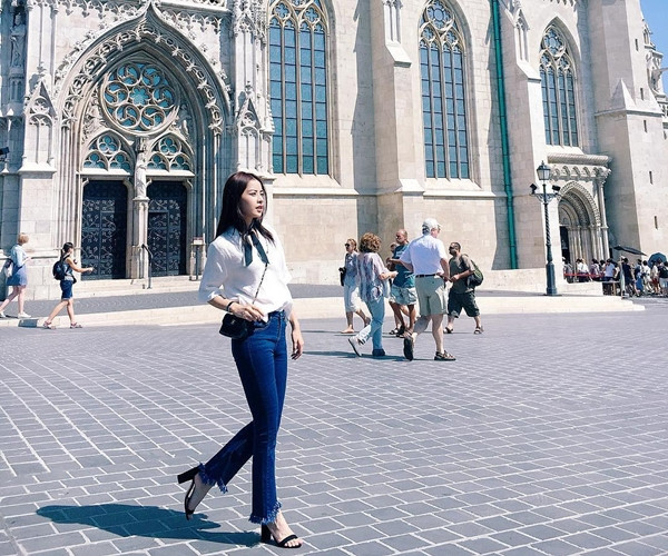 Chi Pu 'thả dáng' trên đường phố Budapest với bộ đồ được mix tinh tế. Cô nàng kết hợp áo phông trắng cùng quần jeans ống vẩy có gấu tua rua, nhấn nhá phong cách retro bằng chiếc khăn nhỏ buộc cổ.