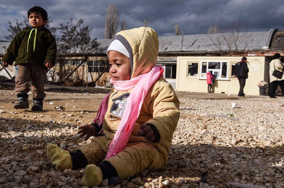Em bé ngồi trên nền đất trong khi người lớn đợi xe buýt ở trạm chung chuyển của Serbia. (Nguồn: Reuters)