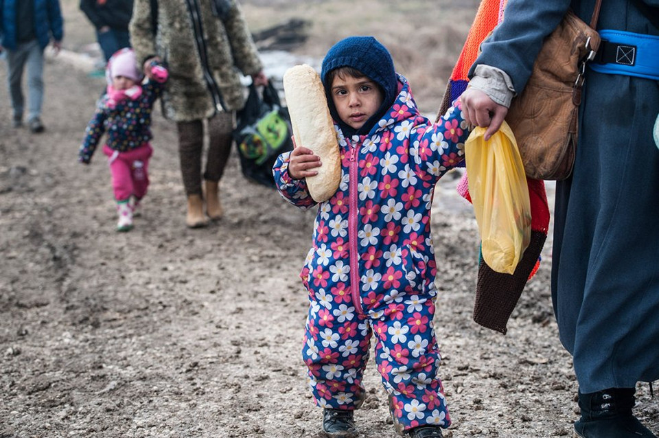 Một em bé đang cầm bánh mỳ trên tay, em đang được người lớn dẫn đi vào biên giới Serbia. (Nguồn: Reuters)