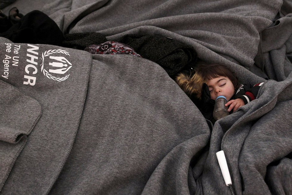 Một em bé ôm bình sữa đi ngủ, chờ đợi được qua biên giới Hy Lạp và Macedonia. (Nguồn: Reuters)