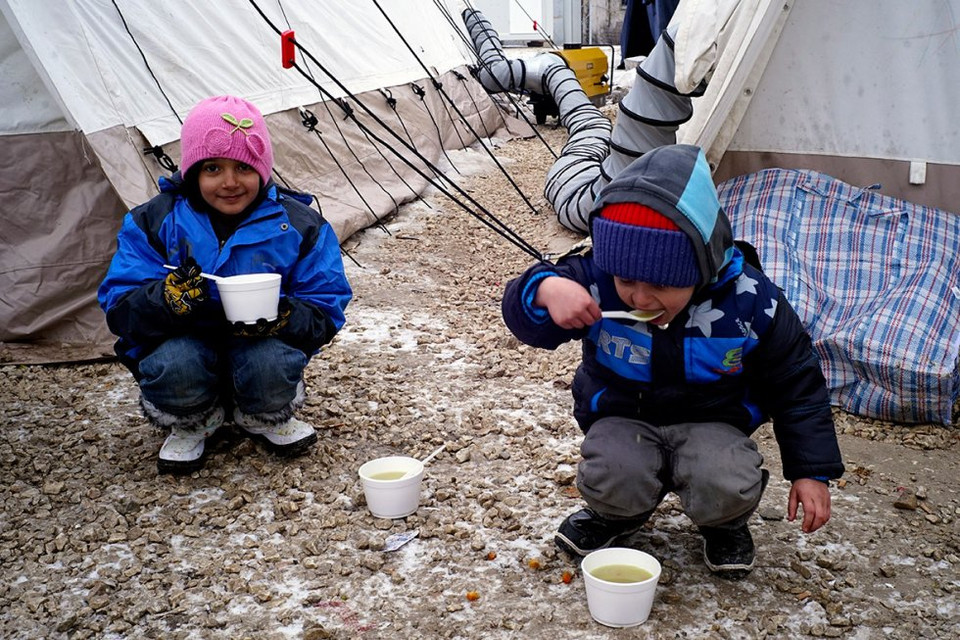 Hai em nhỏ ngồi trên nền tuyết ăn cháo trong trại tị nạn gần biên giới Macedonia và Serbia. (Nguồn: Reuters)