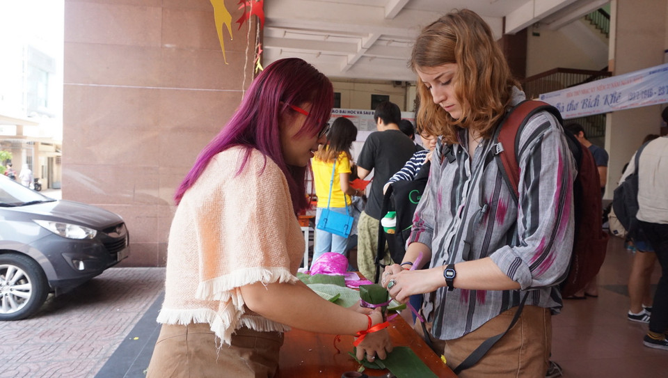 Trần Thị Mai Lan, sinh viên năm ba trường Đại học Khoa học Xã hội và Nhân văn hướng dẫn một bạn sinh viên nước ngoài gói bánh tét. (Ảnh: Lưu Văn Đạt/Vietnam+) 