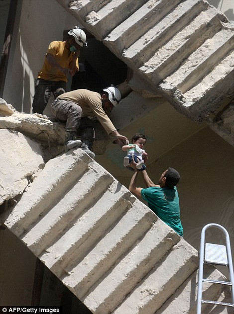 Các tình nguyện viên giải cứu một em bé khỏi đống đổ nát sau cuộc không kích. (Nguồn: dailymail)