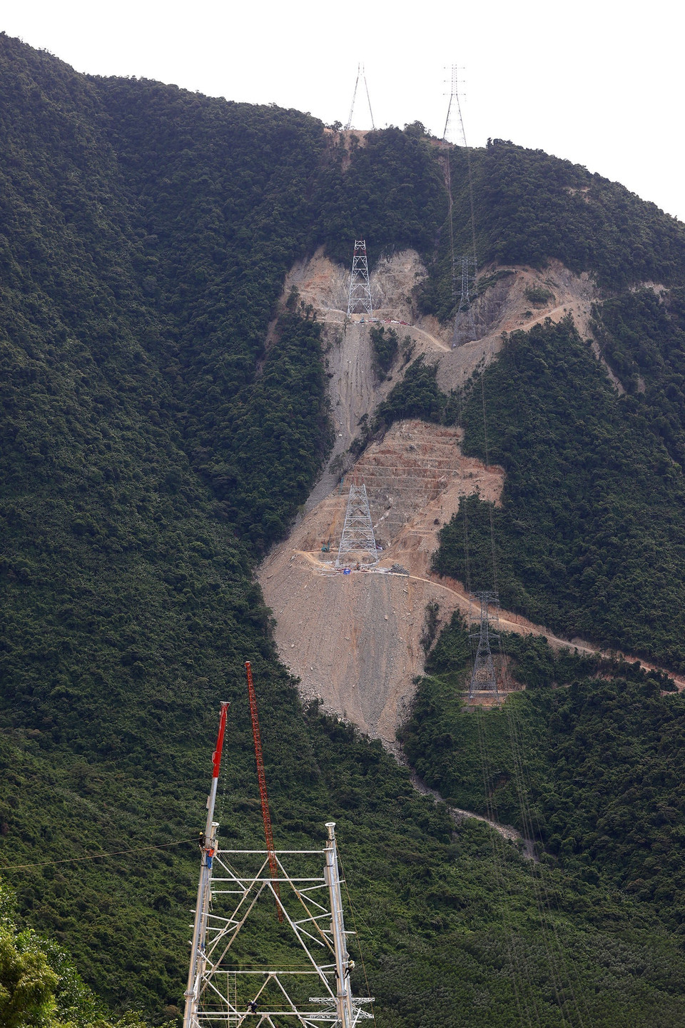 Các vị trí này đều nằm trên vách núi, nên việc vận chuyển thiết bị, nhân lực gặp nhiều khó khăn, chưa kể gió to, gió xoáy khiến cho công tác lắp dựng cột trên cao của công nhân bị cản trở. (Ảnh: Huy Hùng/TTXVN)