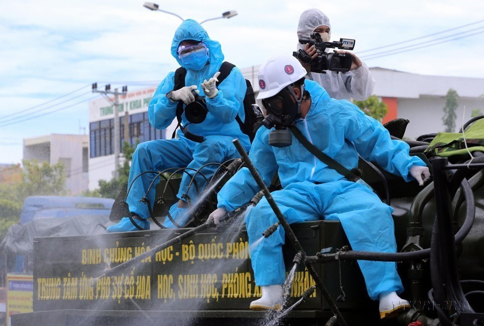 Phóng viên Chi nhánh Trung tâm Truyền hình Thông tấn tại Đà Nẵng tác nghiệp trên thùng xe đi phun thuốc khử trùng các khu vực có nguy cơ lây nhiễm COVID-19 cao trên địa bàn quận Sơn Trà (Đà Nẵng). (Ảnh: Trần Lê Lâm/TTXVN)