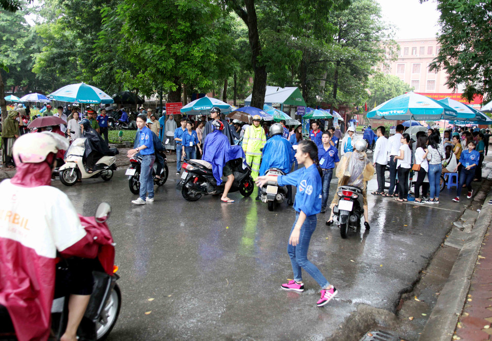 Lực lượng sinh viên tình nguyện, cảnh sát giao thông, cảnh sát trật tự đội mưa đảm bảo giao thông và hướng dẫn các thí sinh làm vào thủ tục thi. (Ảnh: Doãn Đức/Vietnam+)