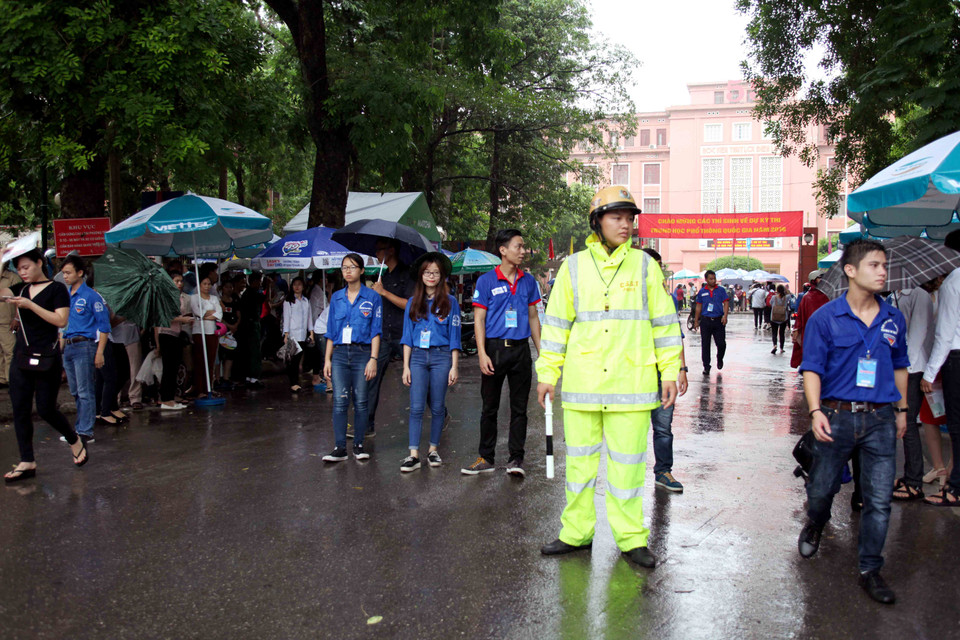 Lực lượng sinh viên tình nguyện, cảnh sát giao thông, cảnh sát trật tự đội mưa đảm bảo giao thông và hướng dẫn các thí sinh làm vào thủ tục thi. (Ảnh: Doãn Đức/Vietnam+)