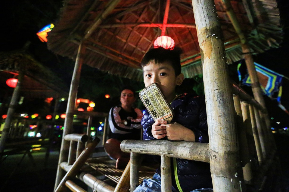 Các em nhỏ rất thích thú khi được bố mẹ cho trải nghiệm ngồi chòi tre xem diễn xướng nghệ thuật Bài Chòi ở phố cổ Hội An. (Ảnh: Trọng Đạt/TTXVN)