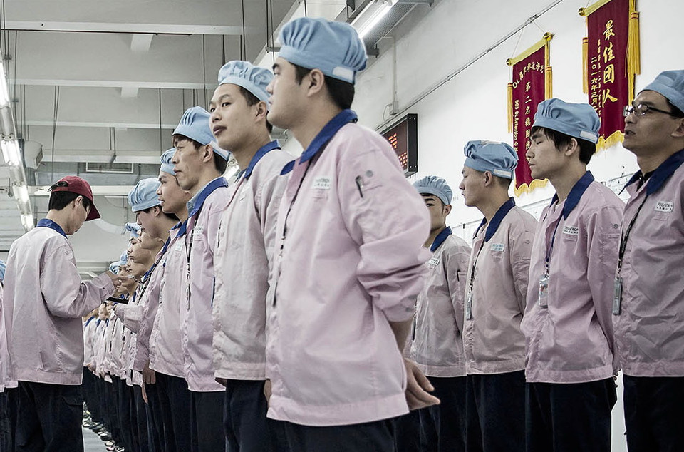 Quản đốc kiểm tra trang phục và điểm danh công nhân trước khi vào làm việc. (Nguồn: Bloomberg)