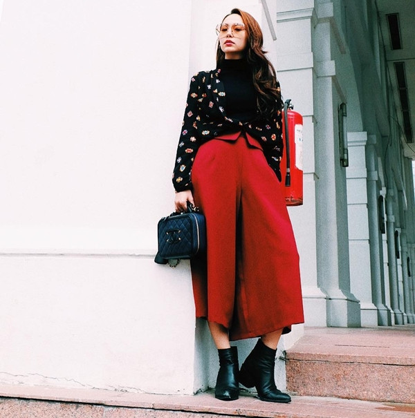 Minh Hằng phối layer áo cổ lọ đen với sơmi họa tiết màu tối, mix ăn ý cùng quần lửng ống rộng tông màu đỏ rực rỡ, tạo nét tương phản. Để nhấn nhá cho bộ cánh street style ngày đầu năm, giọng ca 'Break the rules' còn kết hợp boots da và túi Chanel, mang kính mắt màu sành điệu.