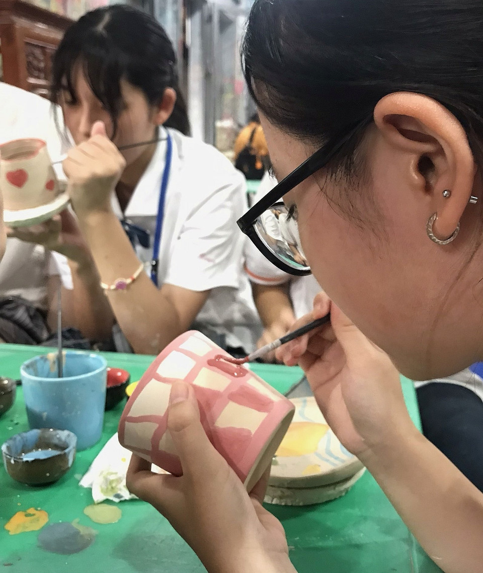 Nữ sinh tỉnh Fukuoka (Nhật Bản) trải nghiệm vẽ hoa văn lên gốm khi tham quan Làng nghề Bát Tràng. (Ảnh: TTXVN phát)