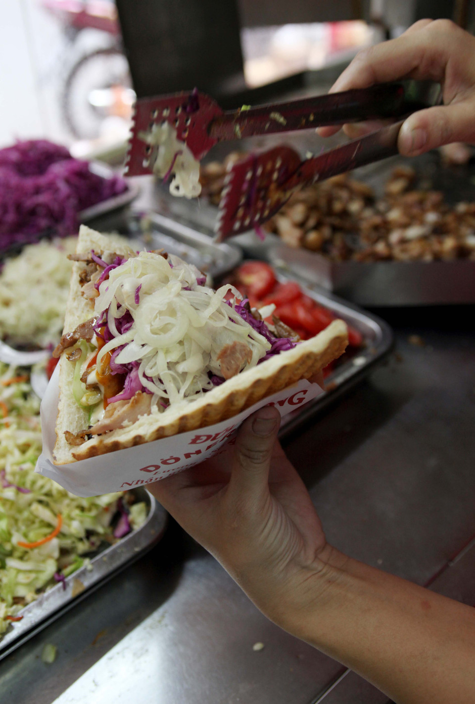 Khi ăn, nhân thịt kẹp cho vào bánh và được đưa vào máy ép nóng, salad ăn kèm cũng khá cầu kì: dưa chuột, cà chua, hành tây và bắp cải tím trộn chua ngọt. (Ảnh: Doãn Đức/Vietnam+)