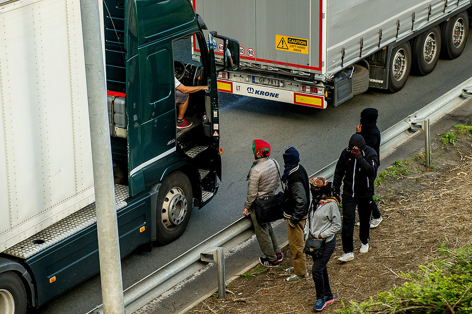 Những người di cư nói chuyện với một người lái xe tải khi đi bộ dọc theo con đường dẫn đến đường hầm Channel ở Coquelles. (Nguồn: AFP)