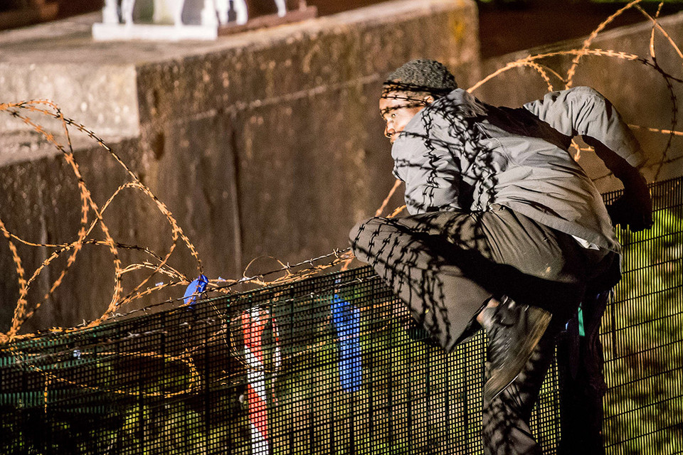 Một người di cư trèo qua hàng rào an ninh để tiến vào đường hầm qua eo biển Manche, do hãng Eurotunnel vận hành, tại Coquelles gần Calais. (Philippe Huguen/AFP)