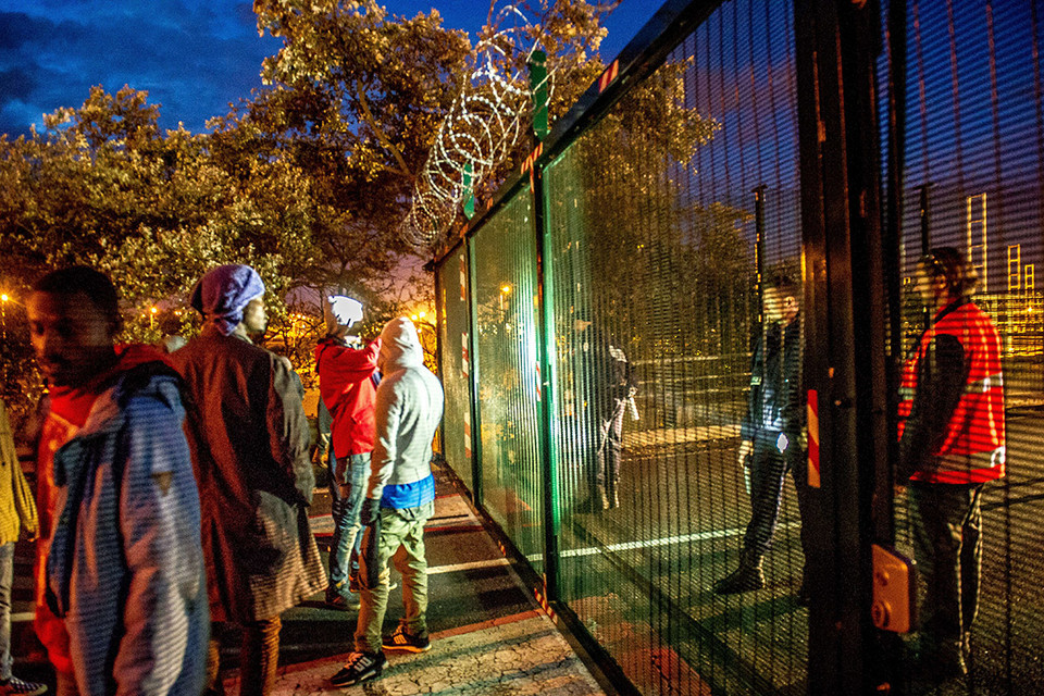 Cảnh sát đứng canh giữ khu vực hàng rào để tiến vào đường ray tàu trong khi những người di cư tụ tập ở bên ngoài. (Nguồn: AFP)