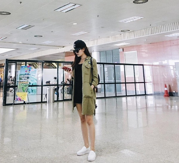 Huyền My gây ấn tượng với thời trang sân bay khỏe khoắn. Á hậu mix đầm đen ngắn cùng áo khoác quân đội, kết hợp giày thể thao và mũ lưỡi trai, tạo sự thoải mái. 