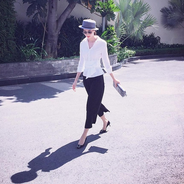 Hoa hậu Đặng Thu Thảo hóa quý cô thanh lịch khi diện sơmi trắng có đai thắt ngang eo cùng quần ống lửng đen. Mỹ nhân 9X phối bộ cánh đơn giản cùng mũ vành tròn và ví cầm tay màu sắc nền nã.