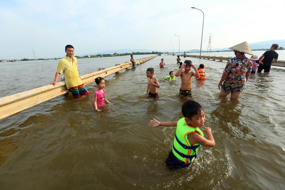 Trẻ em nô đùa tập bơi trên đường tỉnh lộ bị ngập sâu. (Ảnh: Huy Hùng/TTXVN)
