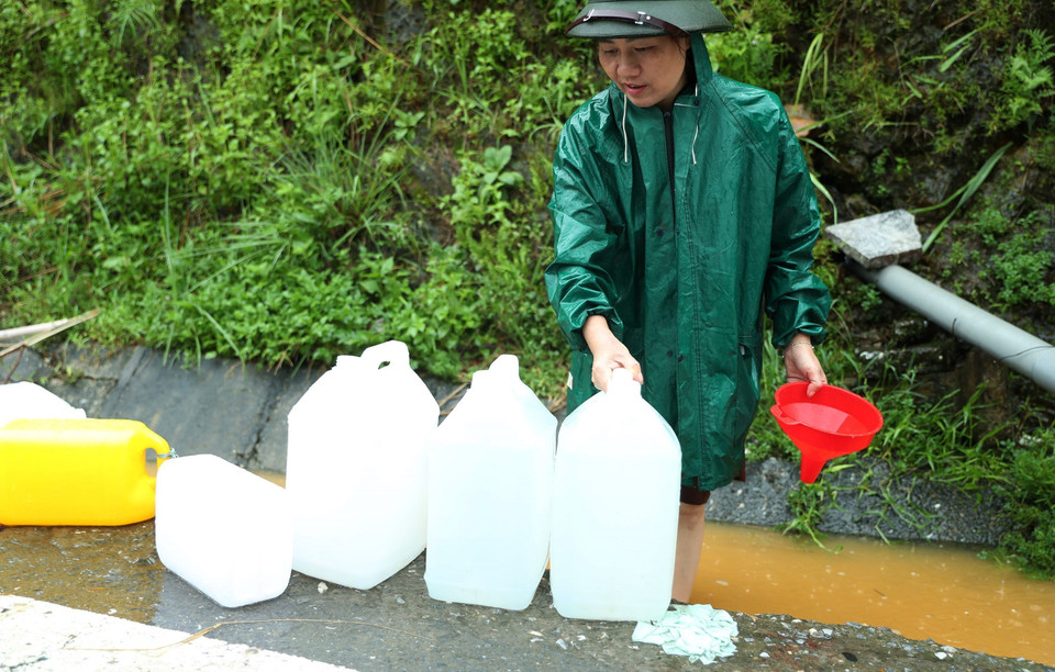 Người dân phường Kim Tân, thành phố Lào Cai đội mưa to, gió lớn để "đong đầy" nước được chảy ra từ khe núi đem về sinh hoạt gia đình. (Ảnh: Quốc Khánh/TTXVN)