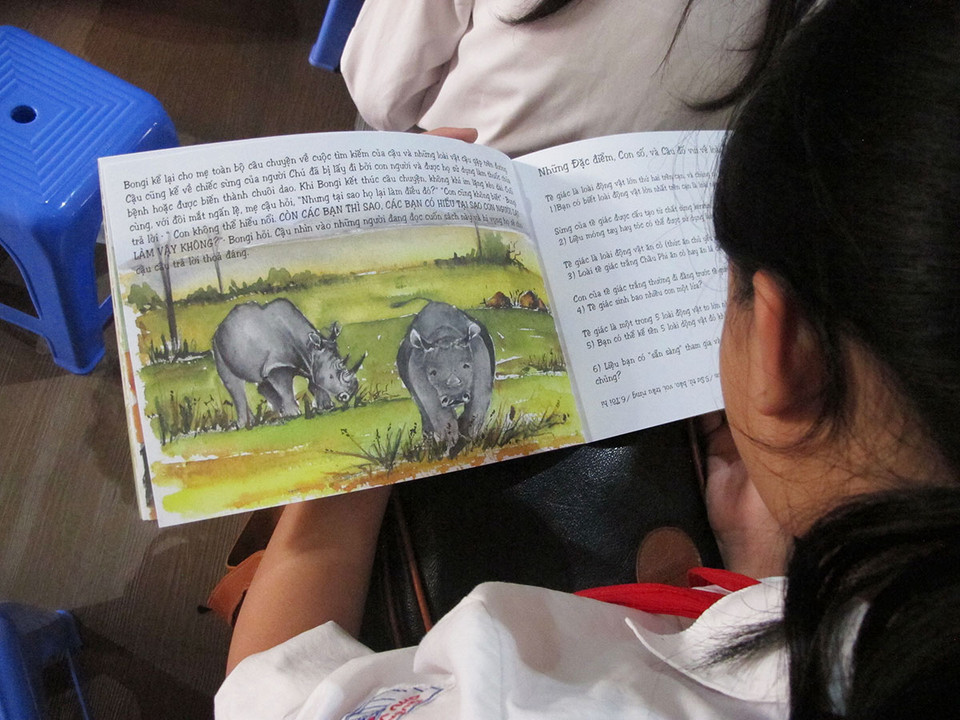 Các em học sinh không thể rời mắt khỏi cuốn truyện 'cuộc phiêu lưu của chú tê giác Bongi,' một món quà đến từ đại sứ quán Mỹ tại Việt Nam. (Ảnh: Tiến Đạt/Vietnam+)