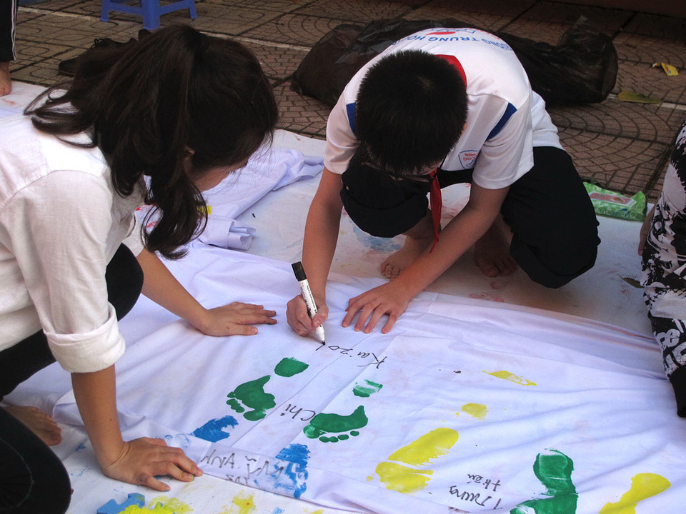 Bên cạnh in dấu chân, các em học sinh còn ký lên đó tên của mình để tăng sức 'nặng' của thông điệp. (Ảnh: Tiến Đạt/Vietnam+) 