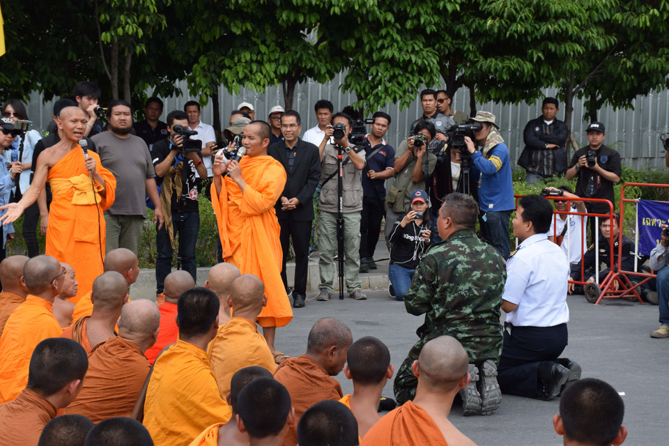 Hai sỹ quan lực lượng bao vây quỳ lạy trước một vị sư thuộc nhóm tín đồ giáo phái Dhammakaya.