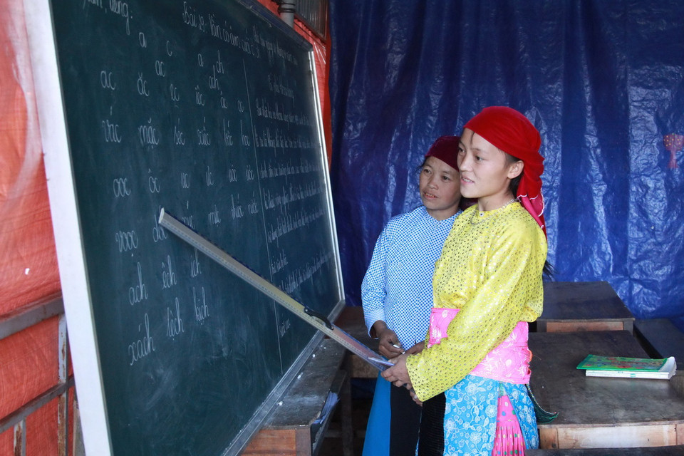 Em Giàng Thị Máy đang hướng dẫn cho chị của mình tập đọc trong lớp học xóa mù ở xã Sảng Tủng, huyện Đồng Văn. (Ảnh: Đỗ Bình - TTXVN) 