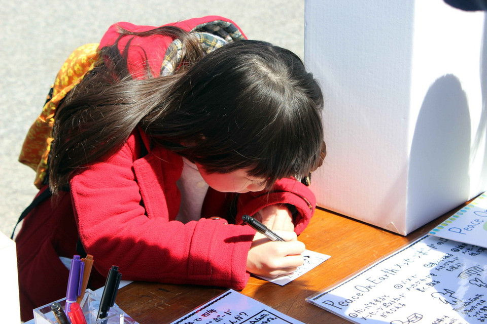 Một em nhỏ viết lời ước nguyện về hoà bình và niềm hy vọng. (Ảnh: Hữu Thắng/Vietnam+)