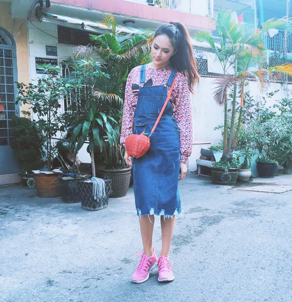 Hương Giang Idol kết hợp áo họa tiết và váy yếm denim xinh xắn. Túi đeo đỏ và giày thể thao hồng mang đến vẻ trẻ trung, tinh nghịch.