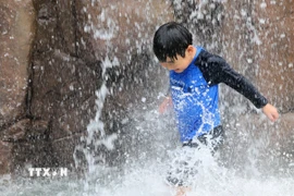 Em nhỏ làm mát dưới đài phun nước ở Incheon, Hàn Quốc ngày 13/7. (Ảnh: Yonhap/TTXVN)