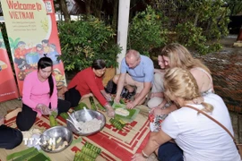 Khách nước ngoài trải nghiệm gói bánh Tét. (Ảnh: Mỹ Phương/TTXVN)