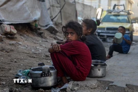 Trẻ em ngồi chờ nhận thức ăn cứu trợ ở thành phố Gaza. (Nguồn: THX/TTXVN)