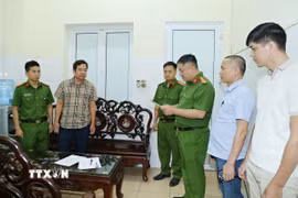 Cơ quan Cảnh sát điều tra, Công an tỉnh khám xét nơi làm việc của Hoàng Văn Huấn (áo kẻ). (Ảnh: TTXVN phát)