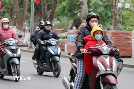 Người dân mặc áo khoác dáng dài và quàng khăn ấm khi di chuyển bằng xe máy qua khu vực hồ Hoàn Kiếm. (Ảnh: Vũ Quang/TTXVN)